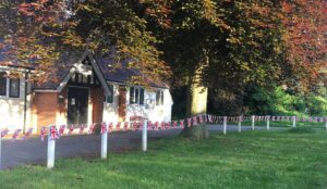 Callow End Village Hall, a white-rendered hall with a timbered gable porch, under a copper beech, with Union Jack bunting strung along the white fence posts in front